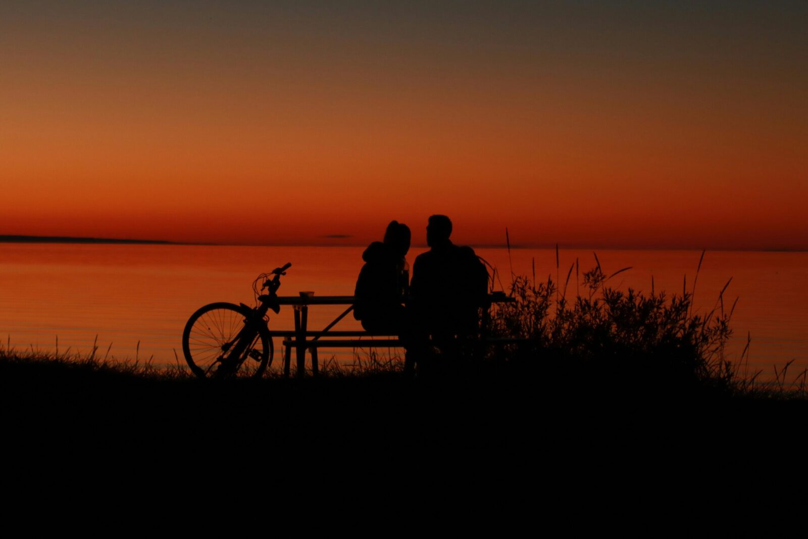 Couple sits at sunset with a bike by the serene shore in Jönköping, Sweden.